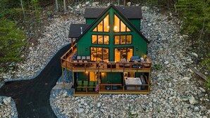 A two-story cabin with a balcony, surrounded by a rocky landscape and trees. - Emerald Escape - Managed by Gr8Escapes (Massanutten)