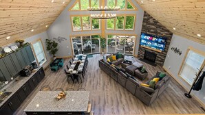 A spacious loft-style living area with a high ceiling, large windows, a fireplace, and a kitchen with granite countertops. - Emerald Escape - Managed by Gr8Escapes (Massanutten)