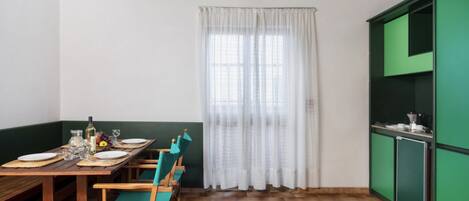 A dining area with a wooden table set for four, green chairs, and a window with white curtains.