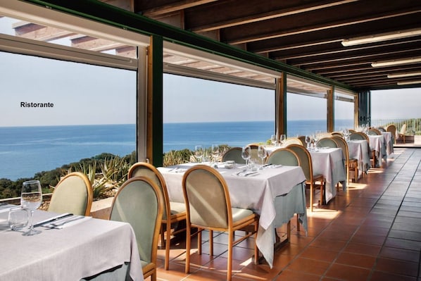 A restaurant with tables set for dining, overlooking a scenic view of the sea.