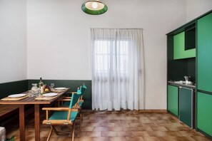 Un comedor con una mesa de madera dispuesta para cuatro, sillas verdes y una ventana con cortinas blancas.
