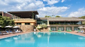 A swimming pool with lounge chairs and umbrellas, surrounded by a building with a stone facade and a covered area.