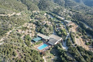 Vista aérea de un complejo turístico con varias edificaciones, una piscina y follaje circundante.