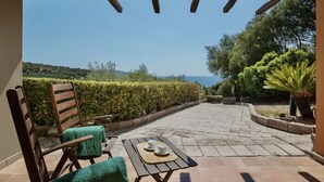 An outdoor patio with a wooden pergola, a table with two cups, and a chair with a green towel.