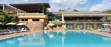 A swimming pool with lounge chairs and umbrellas, surrounded by a building with a stone facade and a covered area.