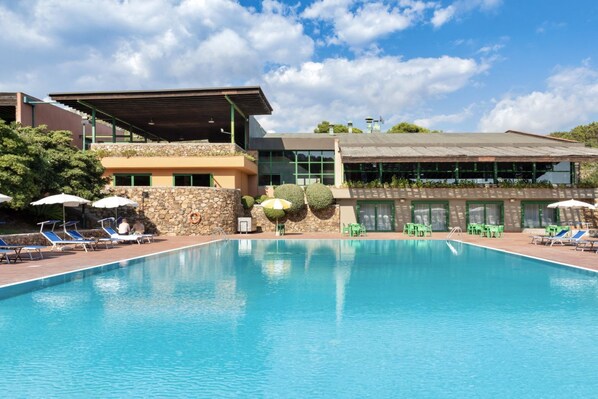 Una piscina con sillas de descanso y sombrillas, rodeada por un edificio de fachada de piedra y un área techada.
