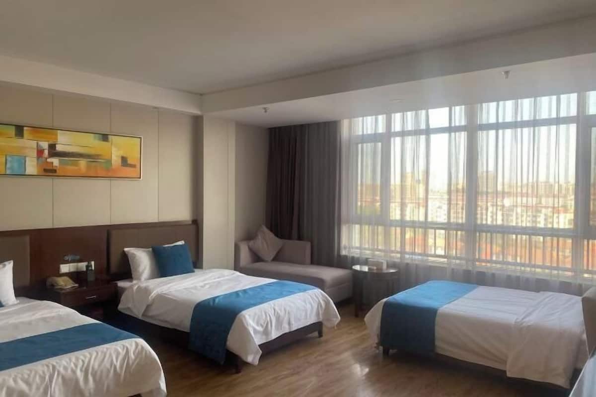 A hotel room with two beds, a sofa, a small table, and a large window with curtains.