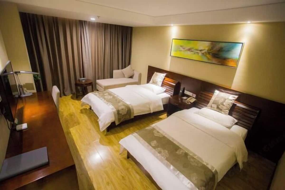 A hotel room with two beds, a desk, a chair, a TV, and a painting on the wall.