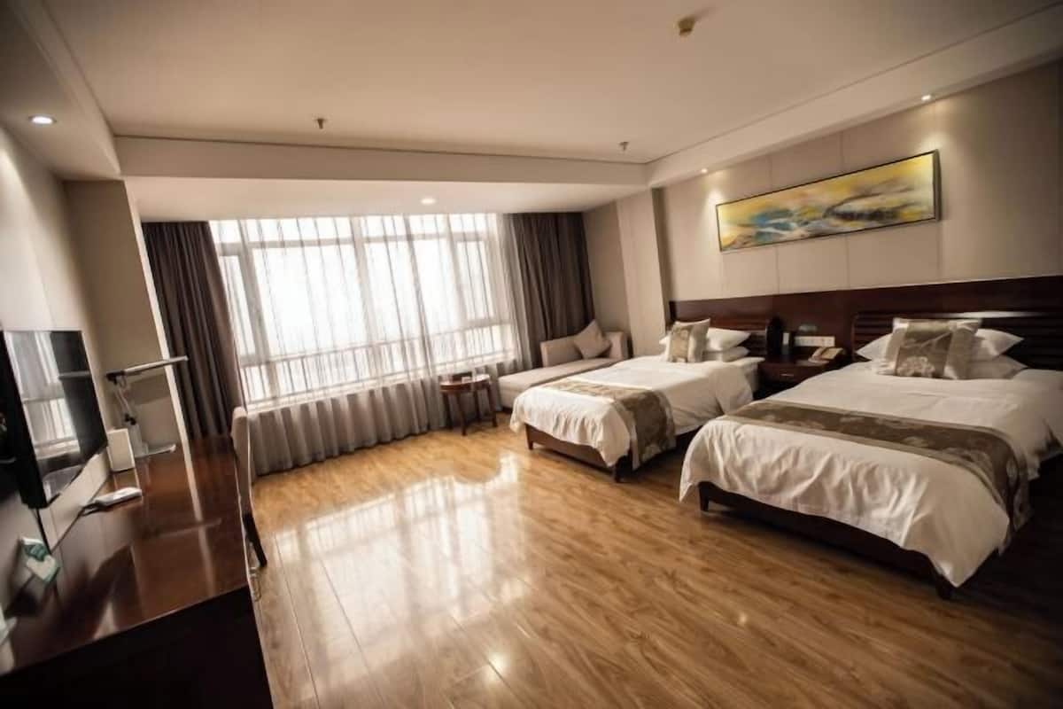 A hotel room with two beds, a TV, a desk, and a large window with curtains.