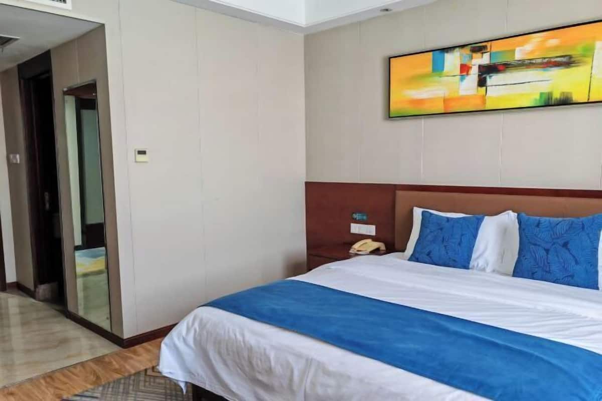 A hotel room with a bed, a painting on the wall, and a telephone on the nightstand.
