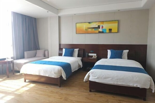 A hotel room with two beds, a large window with curtains, a painting on the wall, and a wooden floor.
