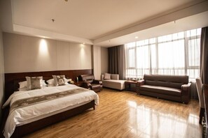 A hotel room with a large bed, a sofa, a chair, and a small table.