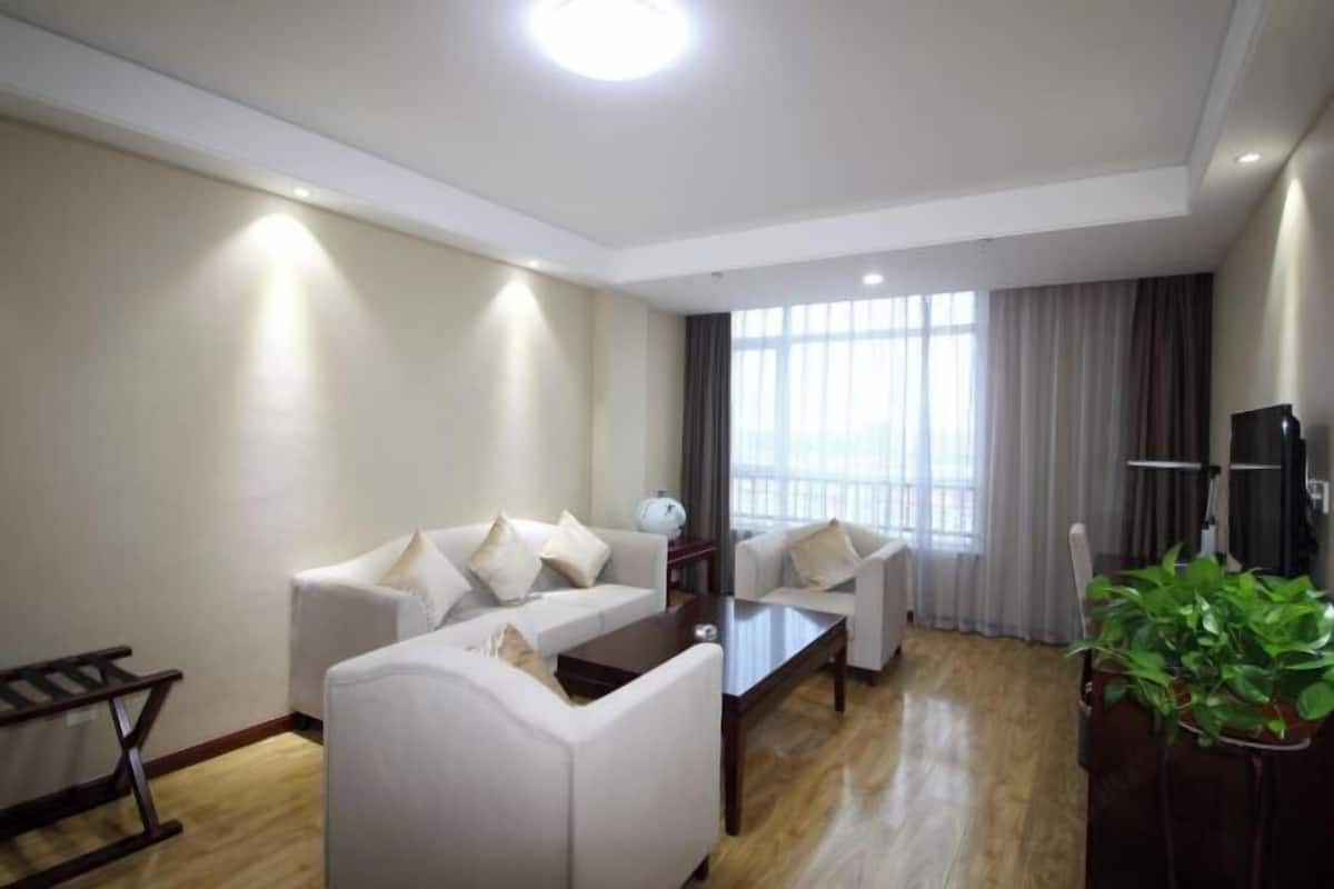 A modern living room with two white sofas, a wooden coffee table, and a large window with curtains.