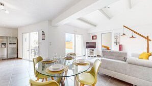 A modern living room with a glass dining table, yellow chairs, a grey sofa, and a TV.