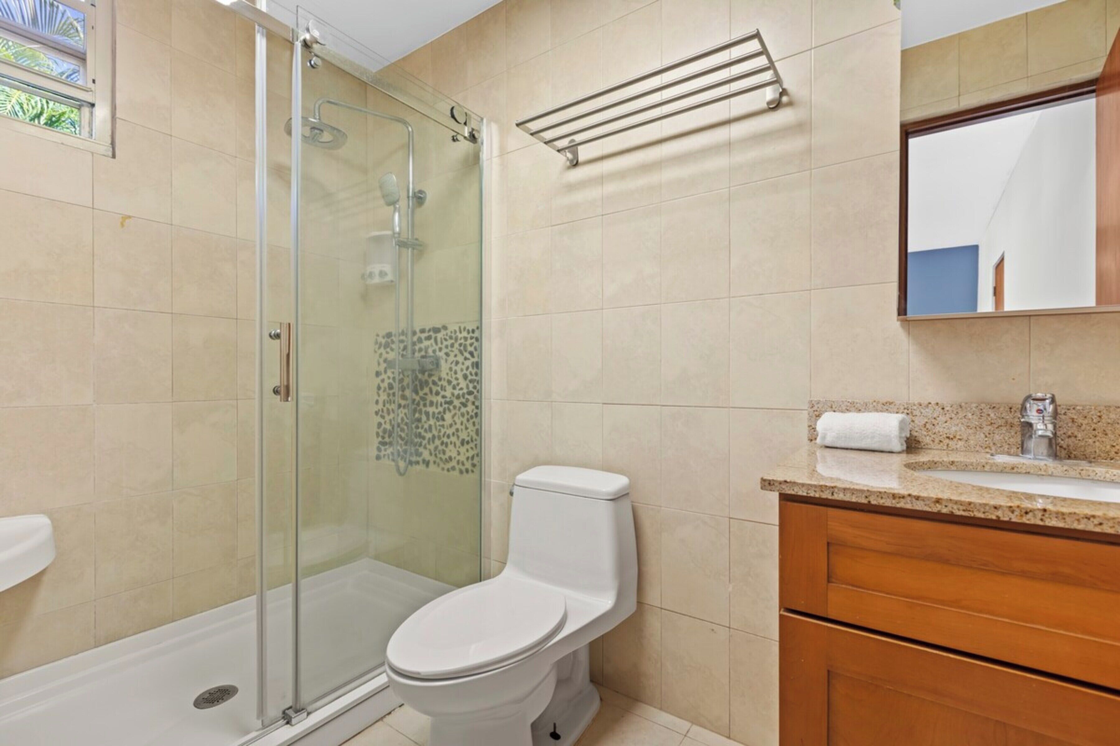 Une salle de bain avec une douche à parois de verre, des toilettes, un lavabo avec un miroir et un porte-serviettes.
