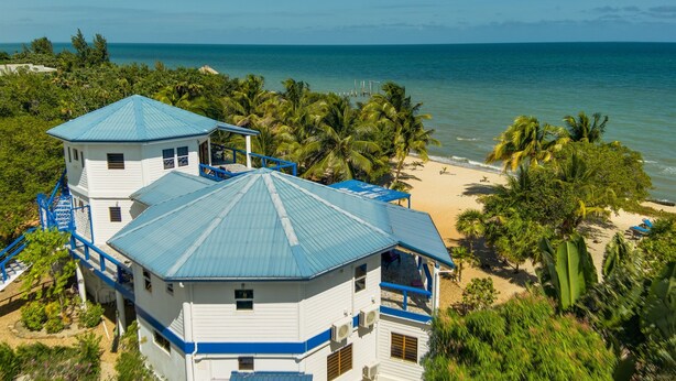 Ein Küstengebäude mit blauem Dach, umgeben von Palmen und einem Strand.