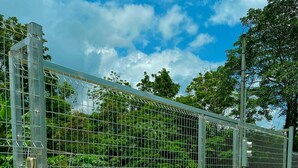 A metal gate with a keypad lock, leading to a paved path surrounded by greenery. - Cabañas El Bosque del Arenal (Peñas Blancas)