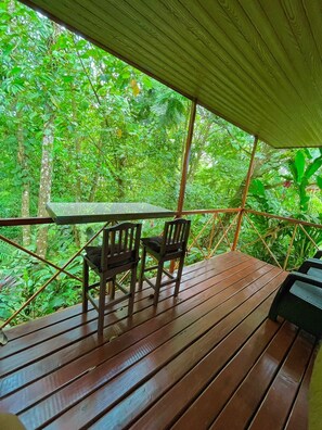 Una terraza de madera al aire libre con una mesa y sillas, rodeada de exuberante vegetación.
