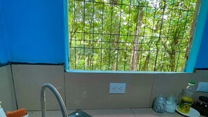 A kitchen with a stainless steel sink, a window with a metal grid, and a view of greenery outside. - Cabañas El Bosque del Arenal (Peñas Blancas)