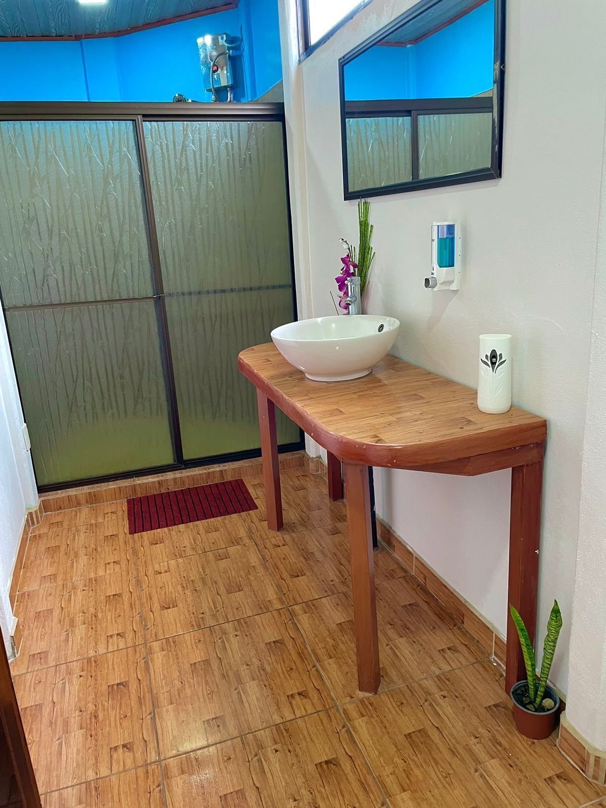 A bathroom with a wooden vanity, a white sink, a mirror, a hand dryer, and a potted plant.