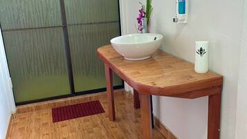 A bathroom with a wooden vanity, a white sink, a mirror, a hand dryer, and a potted plant.