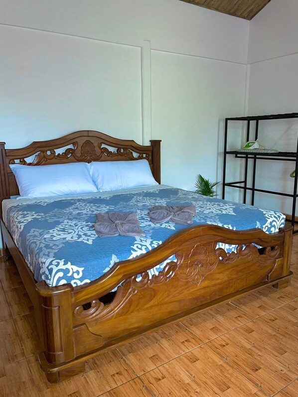 Una cama de madera con colcha de diseño azul y blanco, cabecero de madera y una estantería de metal a un lado.