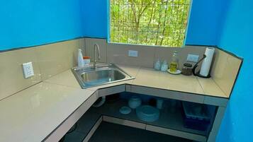 Cocina compacta con pileta, encimera y ventana con vista a follaje.