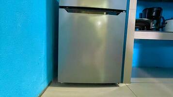 Una cocina compacta con un refrigerador de acero inoxidable, una cafetera y una estantería.