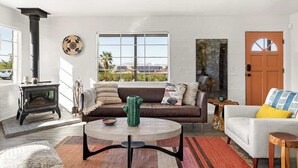 A living room with a fireplace, a sofa, a coffee table, and a view of the outdoors. - Casa Homestead Hemel| Pool | Downtown 29 Palms (Twentynine Palms)