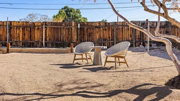 A fenced outdoor area with two wicker chairs and a table. - Casa Homestead Hemel| Pool | Downtown 29 Palms (Twentynine Palms)