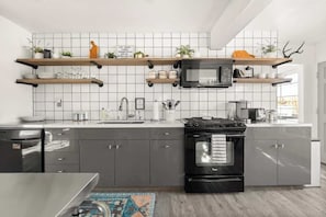 A modern kitchen with a black stove, stainless steel appliances, and wooden shelves with plants.
