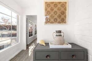 A room with a large window, a decorative wall piece, a woven vase, and a small shell.