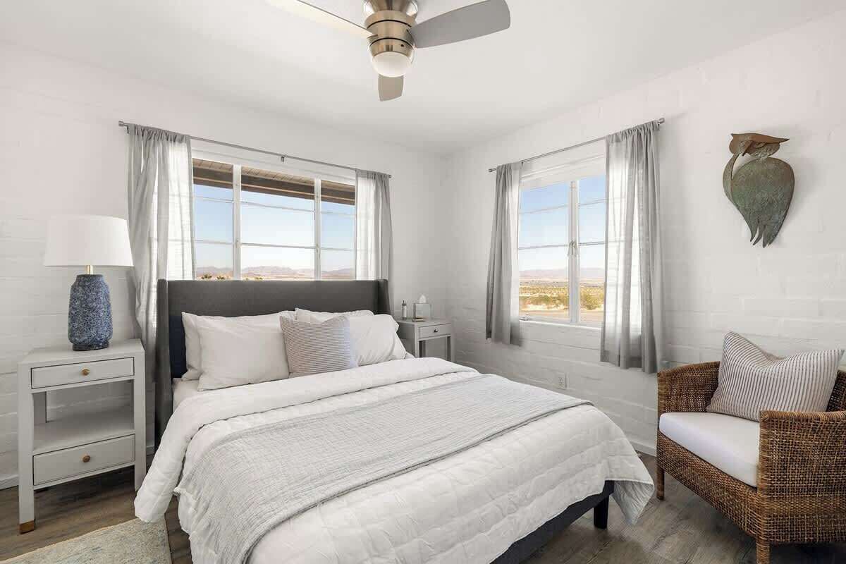 A bedroom with a bed, nightstands, a chair, and a view of the outdoors.