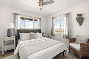 Une chambre à coucher avec un lit, des tables de chevet, une chaise et une vue sur l’extérieur.