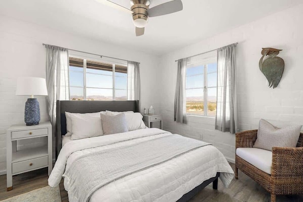 A bedroom with a bed, nightstands, a chair, and a view of the outdoors.