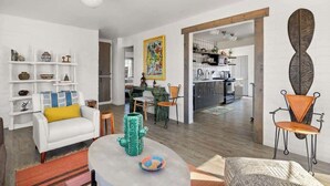 A modern living room with a white sofa, a coffee table, and a dining area with a patterned rug. - Casa Homestead Hemel| Pool | Downtown 29 Palms (Twentynine Palms)