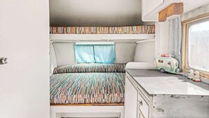 A compact RV interior with a bed, a window, and a kitchenette area. - Casa Homestead Hemel| Pool | Downtown 29 Palms (Twentynine Palms)