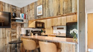 A kitchen with wooden walls, a bar area with two stools, a microwave, a refrigerator, and a coffee maker. - Lichenhearth 09 (Snowmass Village)