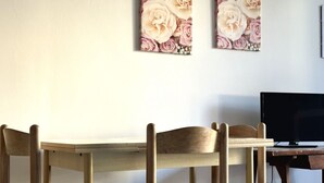 En matplats med ett träbord och stolar, en tv på ett träställ och två väggdekorationer med blommotiv.