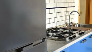 Ett kök med en gasspis, en diskho i rostfritt stål och blå skåp.