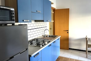 A kitchen with blue cabinets, a gas stove, a microwave, and a refrigerator.