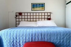 A bed with a blue quilt, a wooden headboard, and a red pillow.