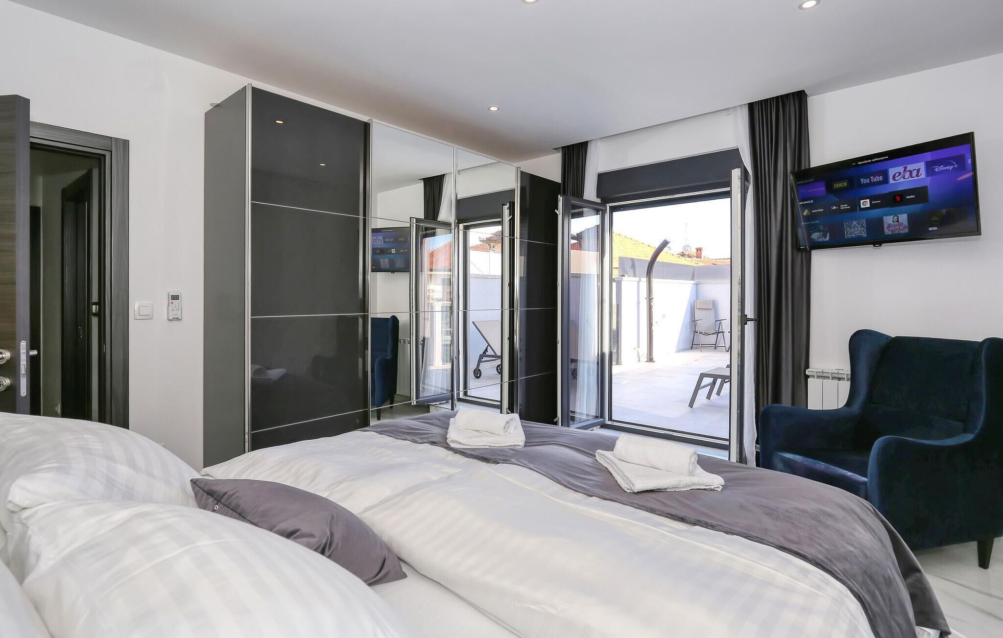 Ein modernes Hotelzimmer mit einem großen Bett, einem an der Wand befestigten Fernseher und einer Schiebeglasdoor zum Außenbereich.