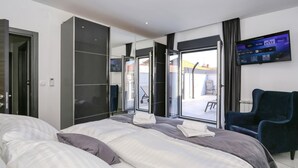 Una habitación de hotel moderna con una cama grande, un televisor montado en la pared y un ventanal corredizo que da a un espacio exterior.