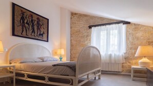 A bedroom with a stone wall, a bed with a woven headboard, a painting, and two bedside lamps. - S339 - Sirolo, wonderful three-room apartment surrounded by nature (Sirolo)