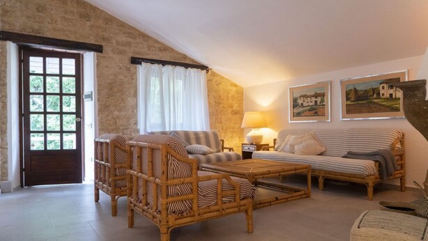 A room with a stone wall, a wooden door, a wicker sofa, a striped sofa, a small table, and two wall-mounted lamps. - S339 - Sirolo, wonderful three-room apartment surrounded by nature (Sirolo)