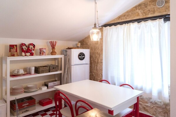 A compact kitchen with a white table, red chairs, a hanging light fixture, and a stone wall.