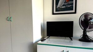 A room with a TV on a cabinet, a fan, and a framed picture on the wall. - Palme 4 - Marcelli, one-room apartment on the ground floor, Residence Le Palme (Marcelli)
