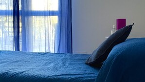 Ein Bett mit blauer Bettdecke, einem Kissen und einem violetten Buch auf einem Nachttisch.