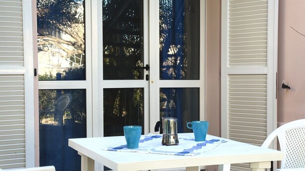 Ein weißer Tisch mit zwei blauen Tassen und einem silbernen Topf, gedeckt auf einer Tischdecke, vor einer weißen Tür mit Fensterfeldern.